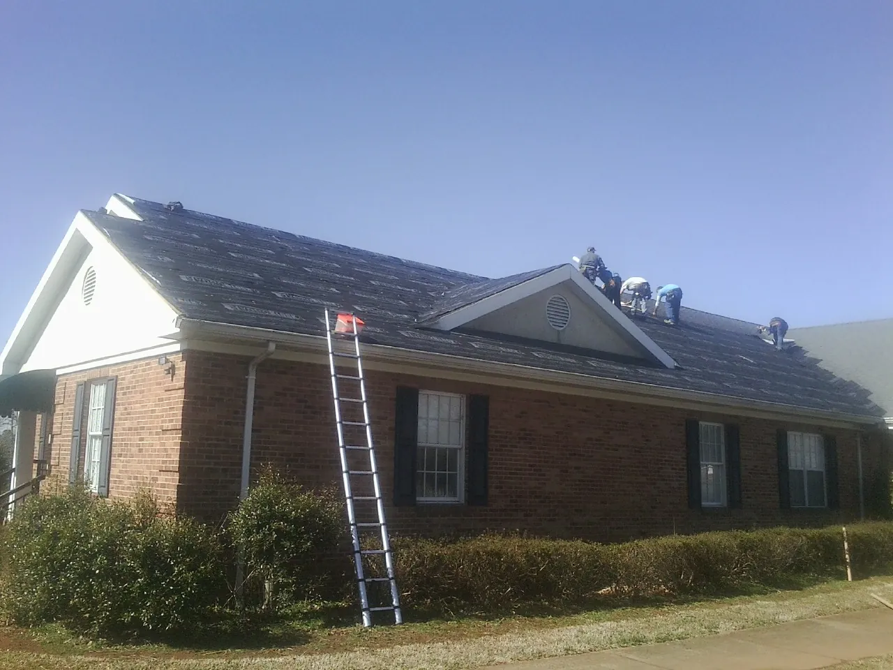 Crew tearing shingles off a brick ranch roof with a ladder set — Emergency Roof Repair work by our crew in Saginaw