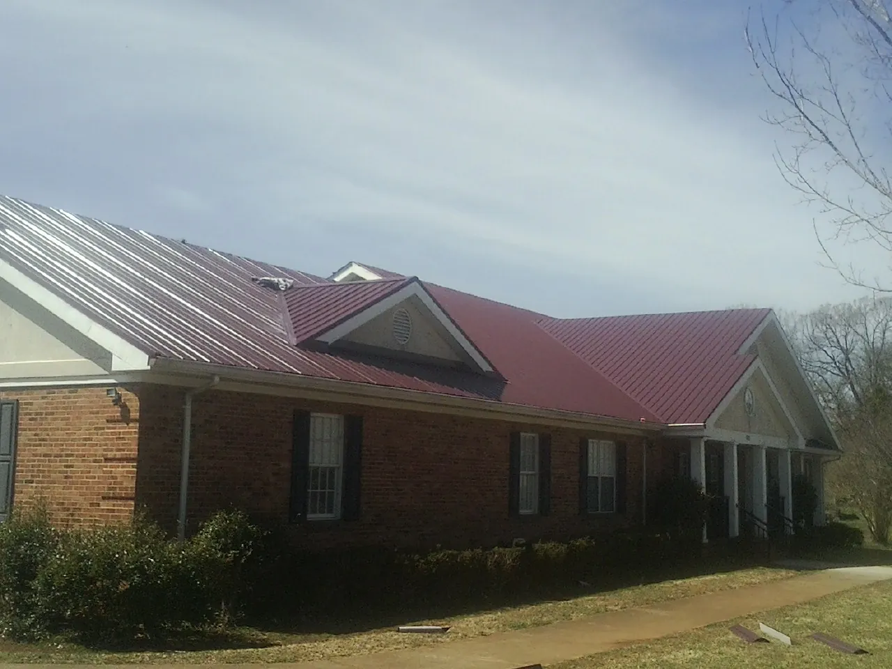 Red metal roof with gabled entries on a long brick building, from a Hail Damage Roof Repair job in Saginaw