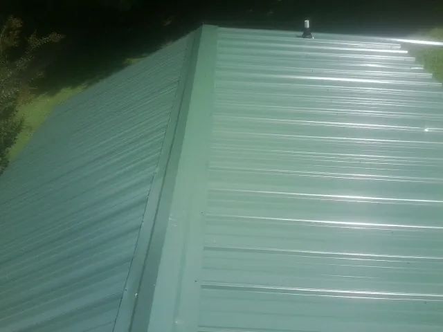 New green metal panels meeting at the ridge of a roof — Flat Roof Repair work by our crew in Saginaw