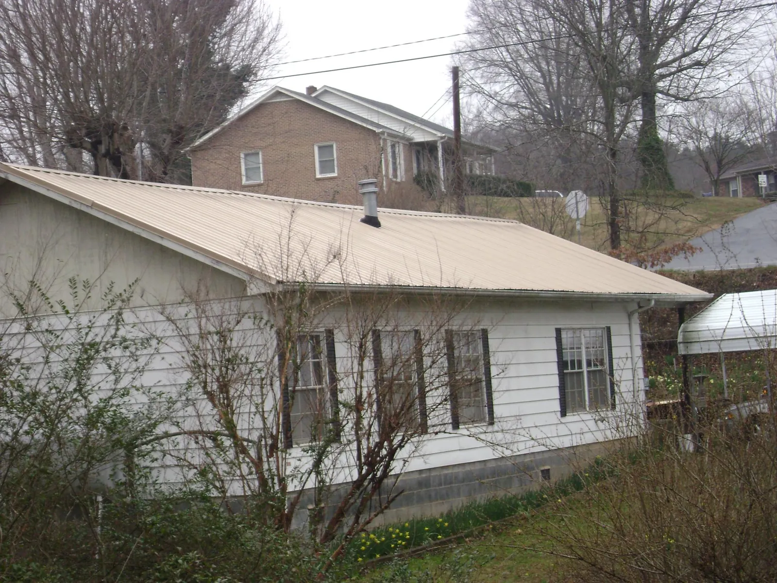 Tan metal roof on a white sided house set into a hillside — Commercial Roofing by Roofing Brothers in Saginaw