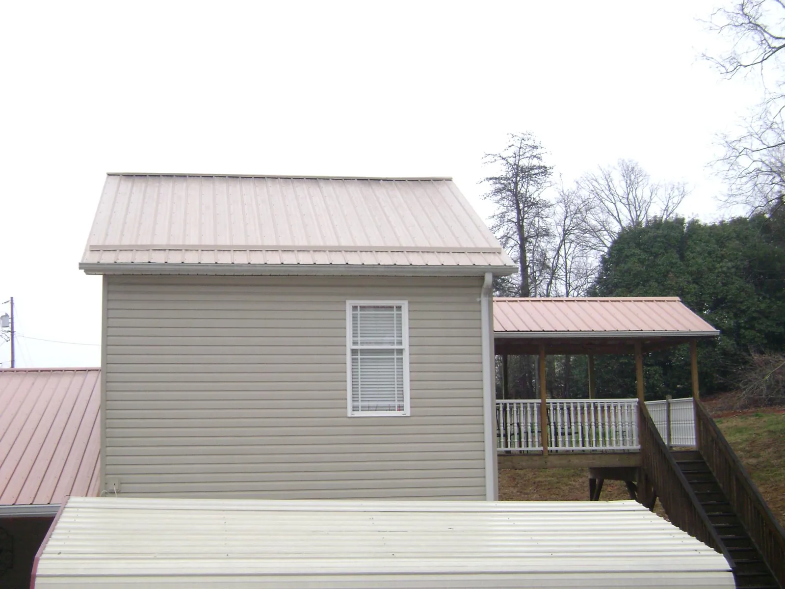 Tan metal roofs on a two story addition and attached porch, from a Roof Replacement job in Saginaw
